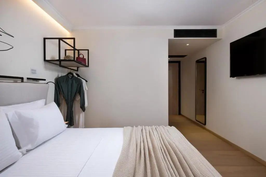 Helles Schlafzimmer mit Doppelbett, beiger Decke und offenem Garderobenelement an der Wand.