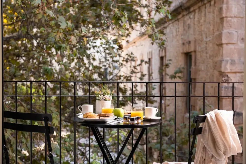 Ein gedeckter Frühstückstisch auf dem Balkon mit Blick auf grüne Bäume und eine Steinwand.