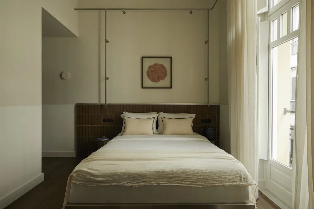 Doppelbett mit hellen Kissen und cremeschimmernder Tagesdecke an einer Holzwand.