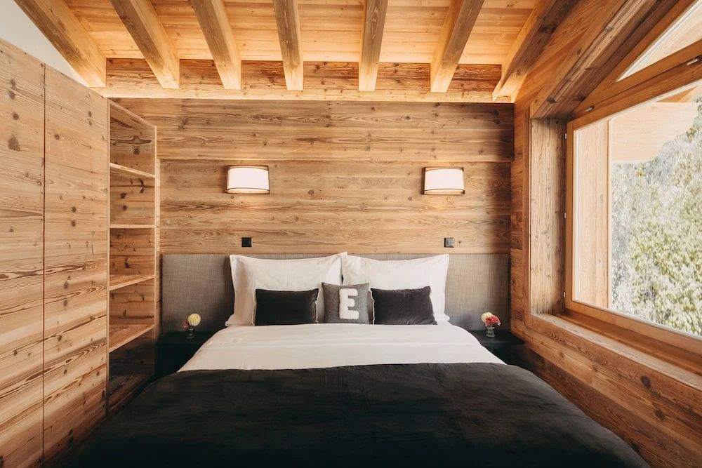 Doppelbett mit Kissen vor einer Holzverkleidung in einem alpenländischen Zimmer.