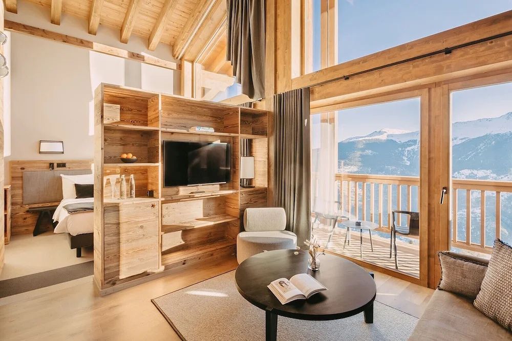 Modernes Wohnzimmer im Holzdesign mit Fernseher, Sessel und Balkon mit Bergblick.