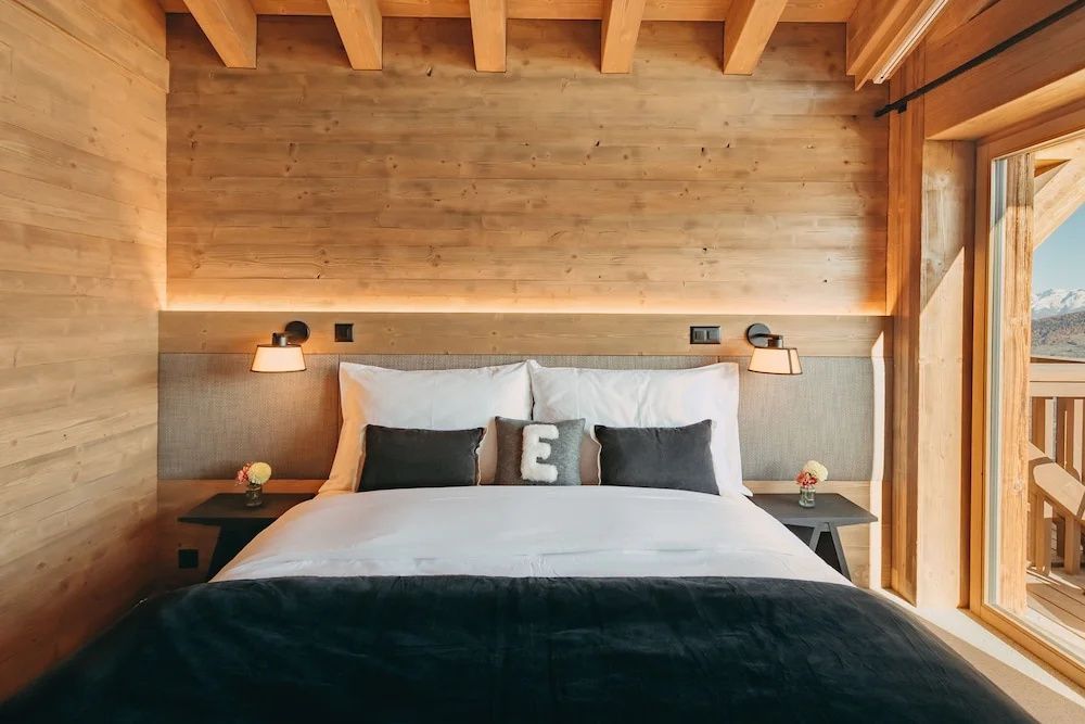 Doppelbett mit weißer Bettdecke, grauen Kissen und beleuchteter Rückwand aus Echtholz.