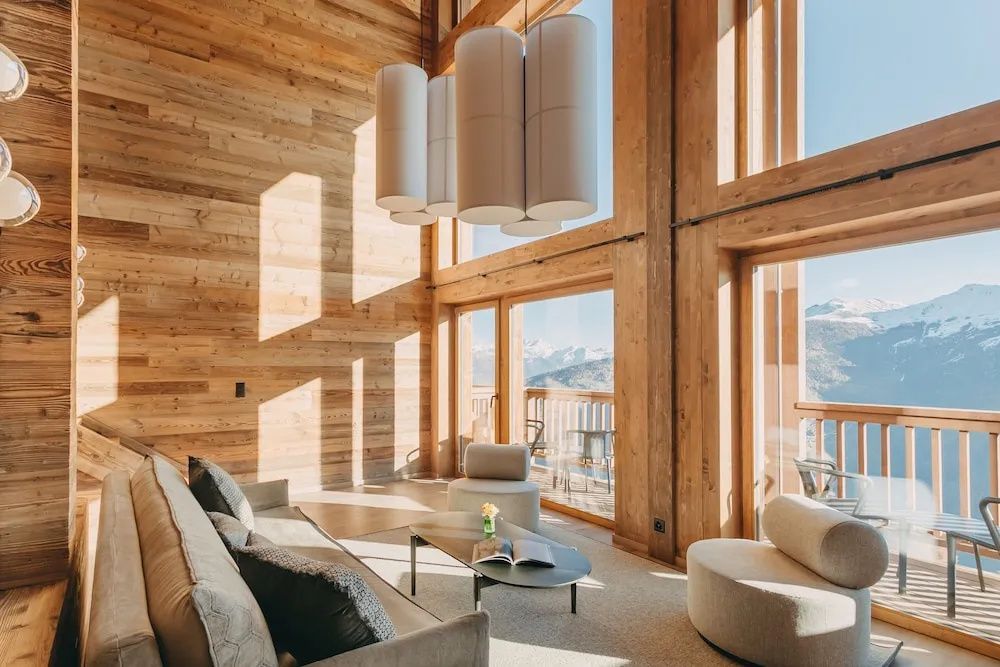 Wohnzimmer mit hoher Holzdecke, großen Fenstern, Sofa und Blick auf die Berge.
