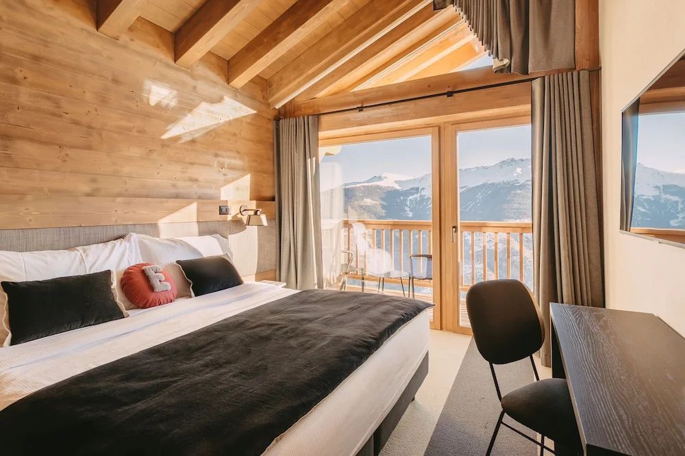 Schlafzimmer mit Holzdecken, gemachtem Doppelbett und großem Fenster mit Bergblick.