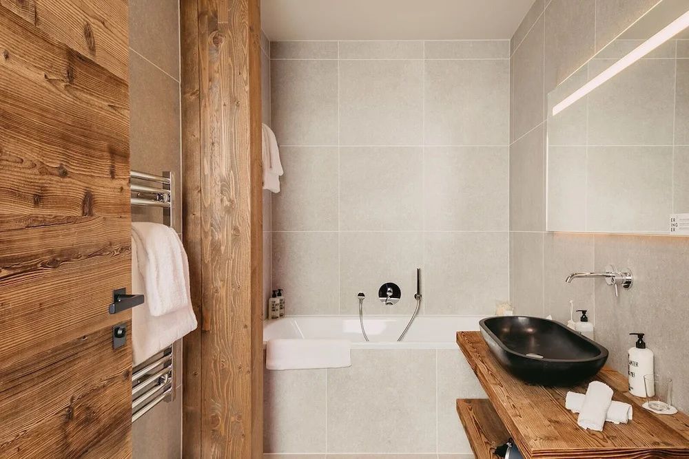Badezimmer mit weiß gefliester Badewanne, dunklem Waschbecken auf Holzplatte und Handtuchwärmer.