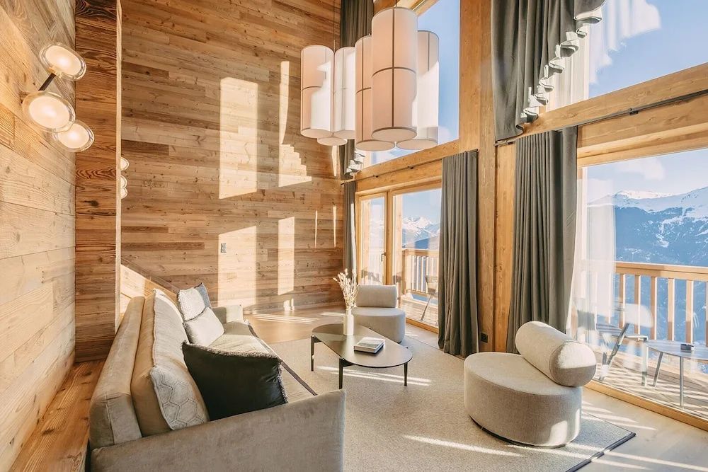 Wohnzimmer im Chaletdesign mit Holzschalung, grauen Vorhängen und Sitzgruppe.