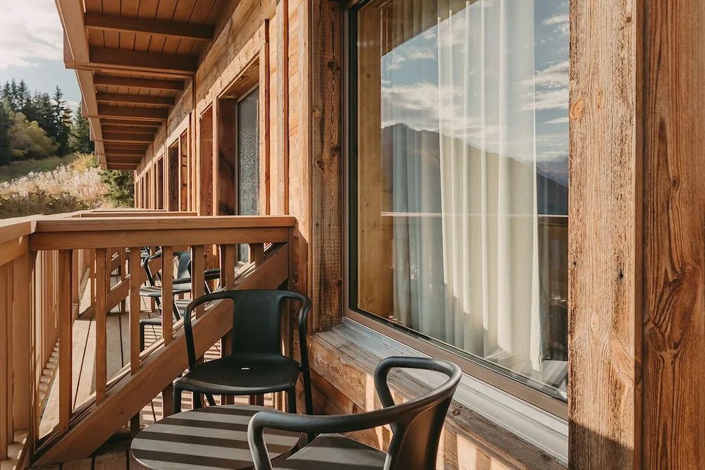 Überdachter Holzbalkon mit zwei schwarzen Stühlen und Blick auf die umliegenden Berge.