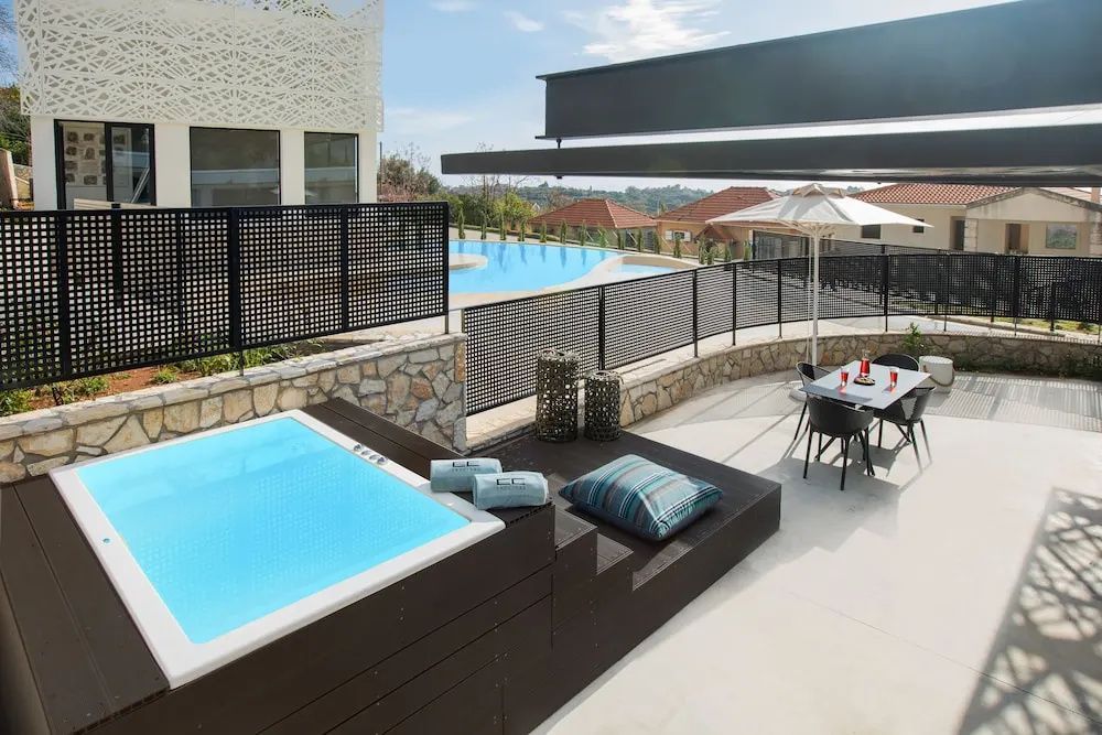 Sonnige Terrasse mit Whirlpool, Sitzgelegenheiten und Swimmingpool im Hintergrund.