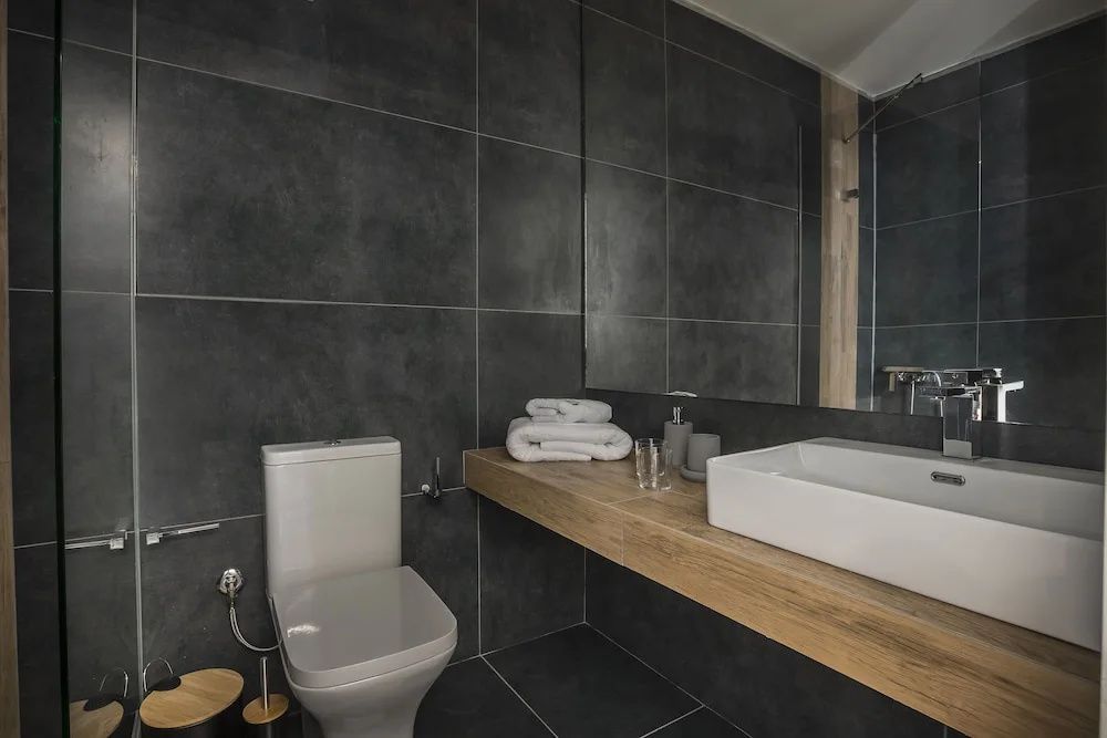 Badezimmer mit dunklen Fliesen, Holzwaschtisch, weißem Waschbecken und einer Toilette.