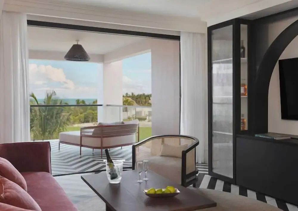 Sitzbereich einer Suite mit Blick auf eine überdachte Terrasse mit Tagesbett und das Meer.