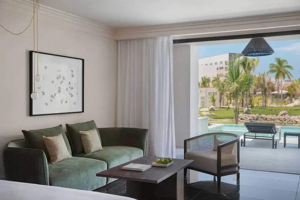 Moderne Suite mit grünem Sofa, Couchtisch und Zugang zur Terrasse im Erdgeschoss.