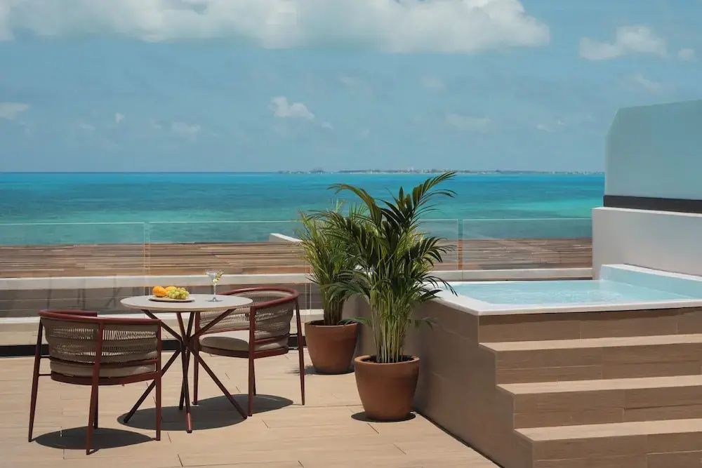 Dachterrasse mit Tisch, Stühlen, Topfpflanzen und Blick auf das türkisblaue Meer.