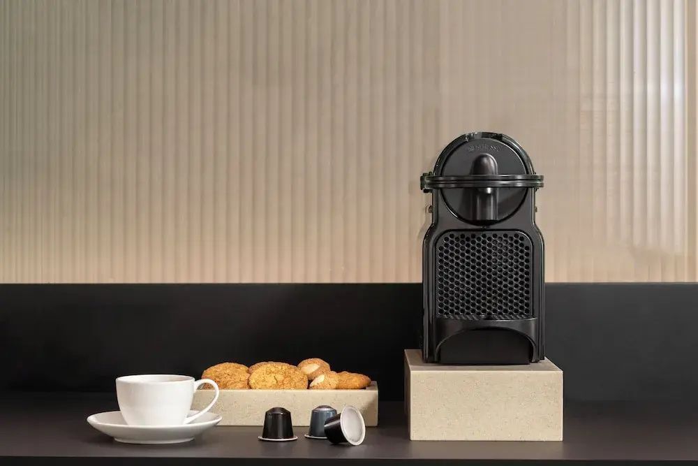 Eine schwarze Kaffeekapselmaschine mit Kapseln, Tasse und Gebäck auf einer Anrichte.