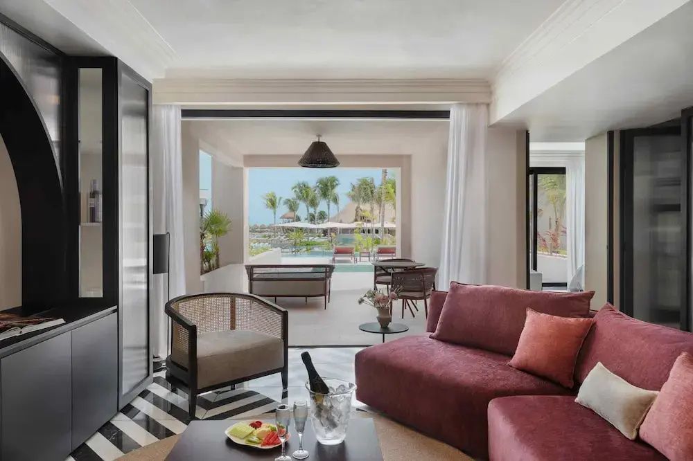 Modernes Wohnzimmer einer Suite mit rotem Sofa, Sessel und Blick auf die Terrasse.