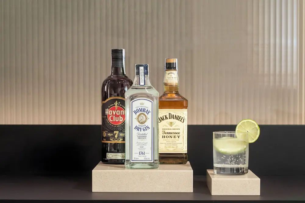 Drei ausgewählte Spirituosenflaschen und ein Drink mit Limette auf einer Ablage.