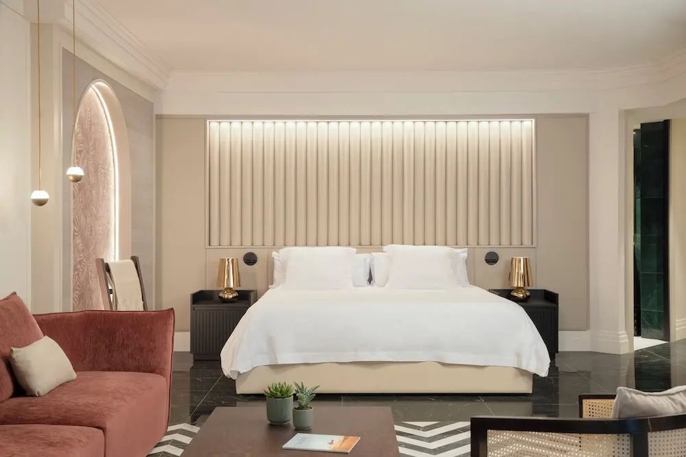 Doppelbett mit weißer Bettwäsche und beigefarbener Wandverkleidung im Hotelzimmer.