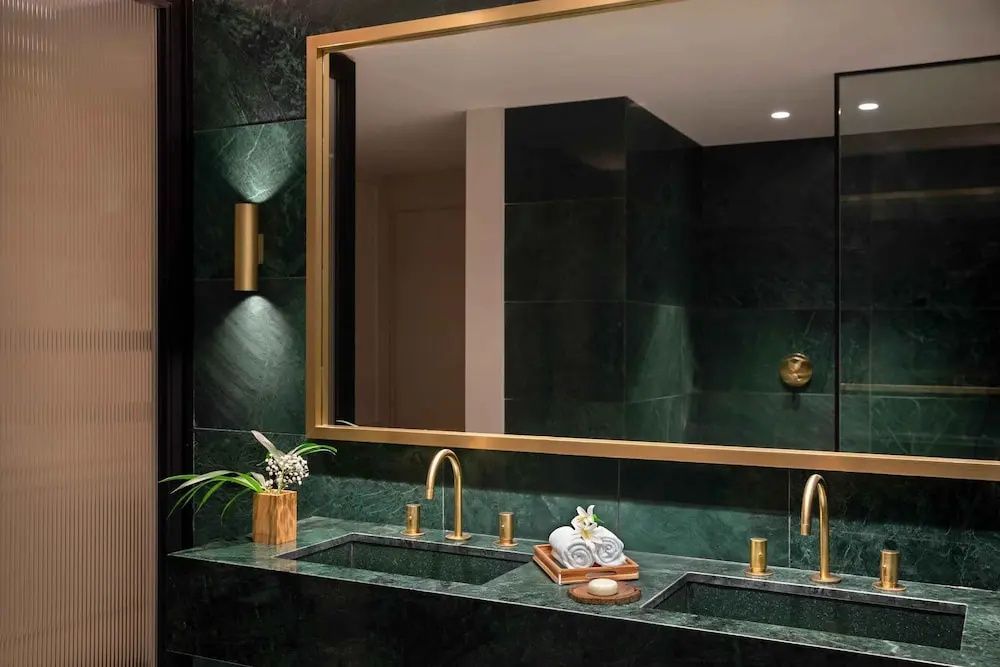 Badezimmer mit grünen Marmorwänden, großem Spiegel und zwei Waschbecken mit Armaturen.