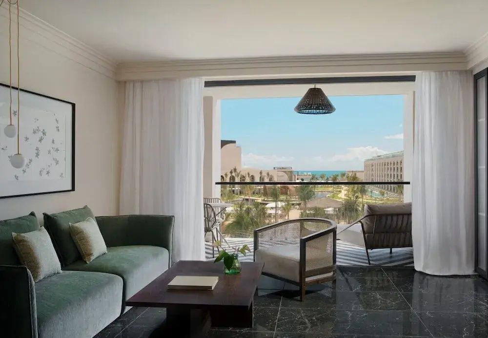 Sitzbereich einer Suite mit Balkon und Ausblick auf die Hotelanlage sowie das Meer.