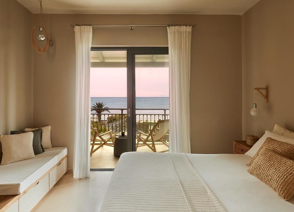 Helles Schlafzimmer im Hotel mit weißem Bett und Durchgang zum Balkon mit Meerblick.
