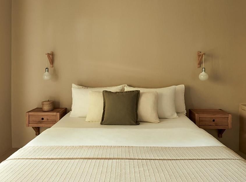 Doppelbett mit hellen Kissen und Nachttischen aus Holz vor beiger Wand.
