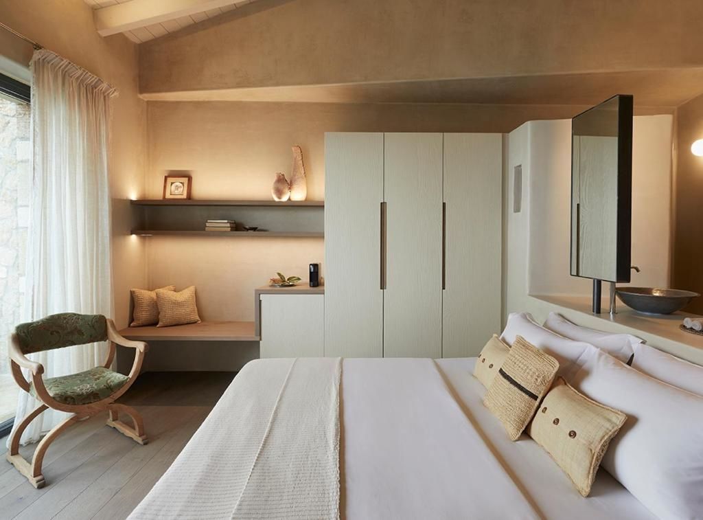 Helles Hotelzimmer mit Doppelbett, Wandschrank, Holzdecke und einer gemütlichen Sitznische im Hintergrund.