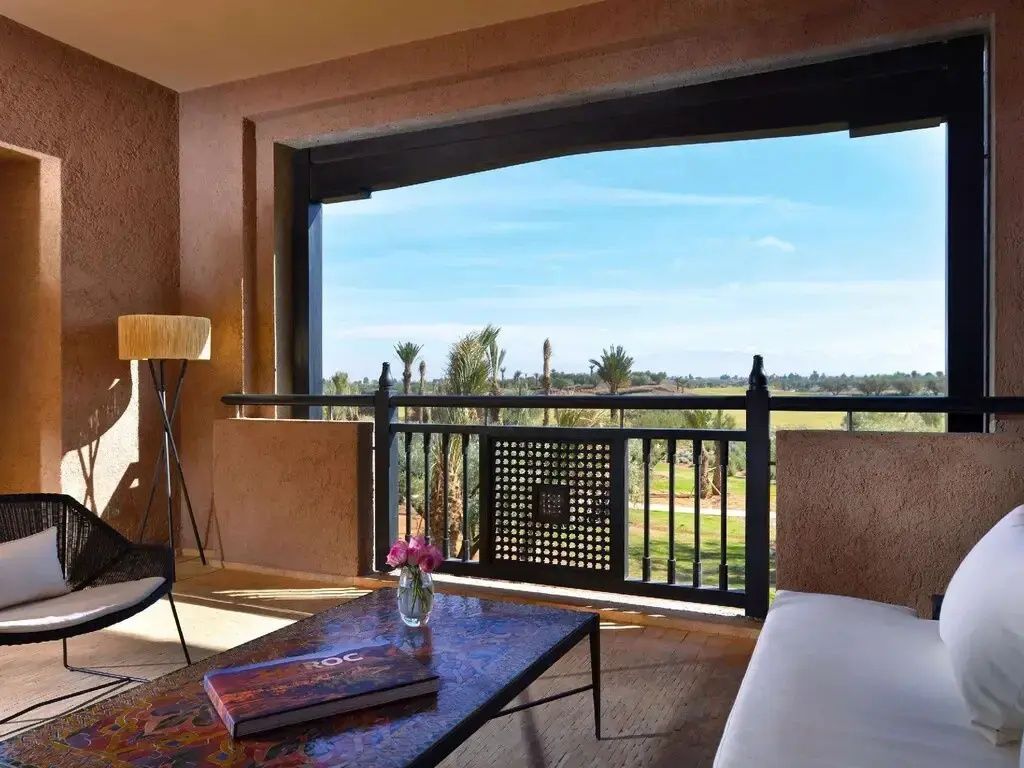 Balkon mit hölzernem Geländer, Tisch und Blick auf Palmen und Landschaft.
