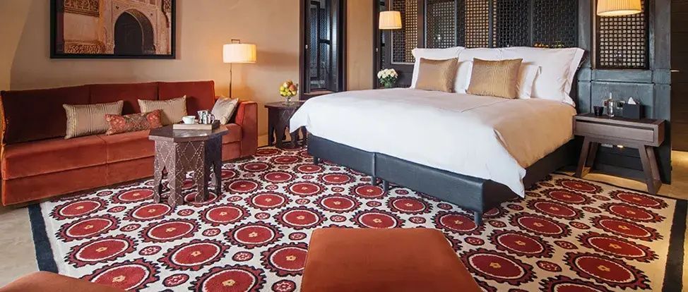 Hotelzimmer mit großem Doppelbett, rot-weiß gemustertem Teppich und Sitzbereich.