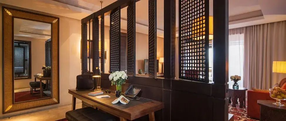 Arbeitsbereich im Hotelzimmer mit Holzschreibtisch, Blumen und orientalischem Raumteiler.