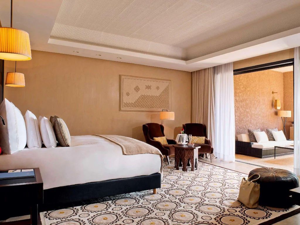 Geräumiges Hotelzimmer mit Doppelbett, gemustertem Teppich und Sitzbereich.