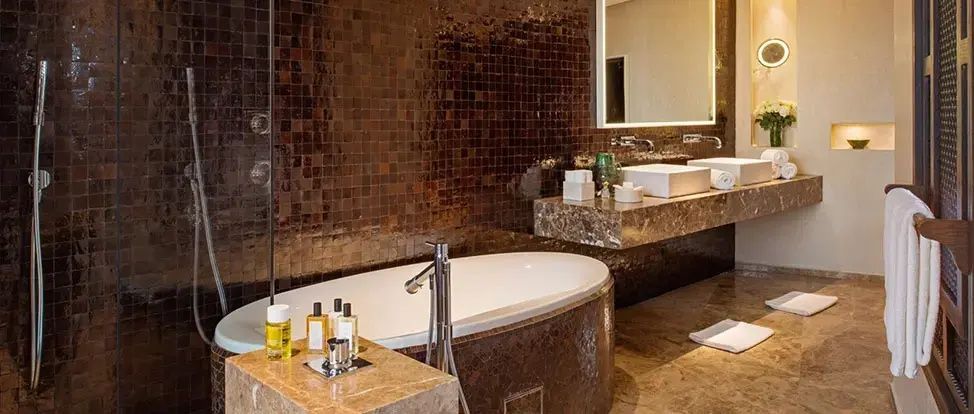 Badezimmer mit dunklen Mosaikfliesen, ovaler Badewanne und Waschtisch aus Marmor.
