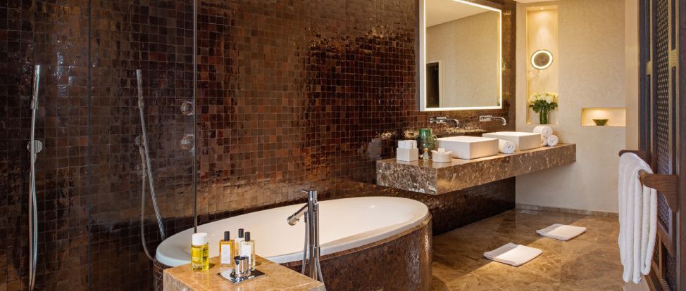 Badezimmer mit einer freistehenden Badewanne, dunklem Mosaik und Waschtisch aus Naturstein.
