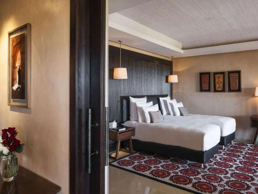 Schlafbereich mit zwei Einzelbetten, Lampen und gemustertem Teppich im Hotelzimmer.