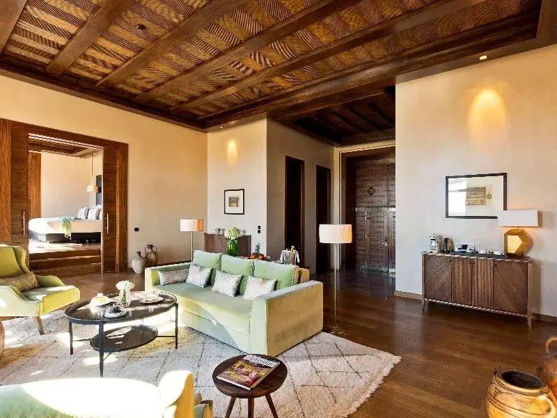 Wohnbereich einer Suite mit grüner Couch, Salontisch, Holzboden und geschnitzter Decke.