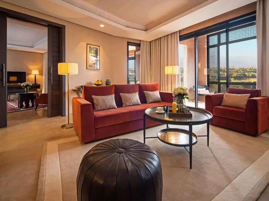 Wohnbereich einer Suite mit rotem Sofa, Couchtisch und Blick ins Freie.