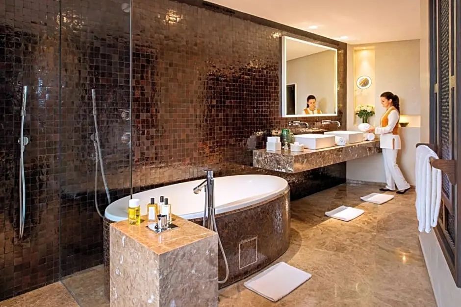 Badezimmer mit frei stehender Badewanne, dunklen Mosaikfliesen und Doppelwaschtisch.