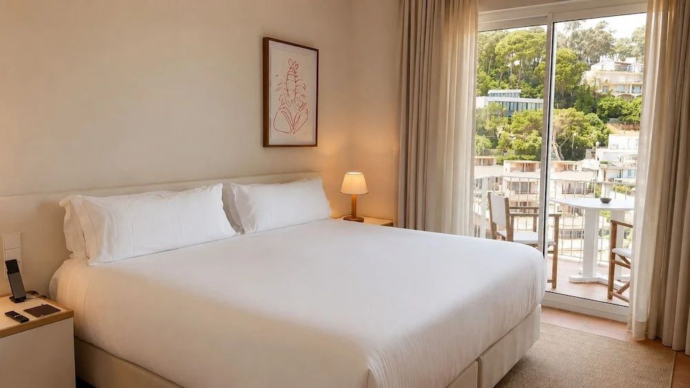 Helles Hotelzimmer mit Doppelbett, Nachttischlampe und Blick ins Grüne