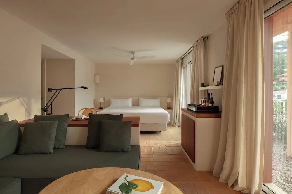 Geräumiges Hotelzimmer mit Doppelbett, Sitzecke und hellen Vorhängen auf Fliesenboden