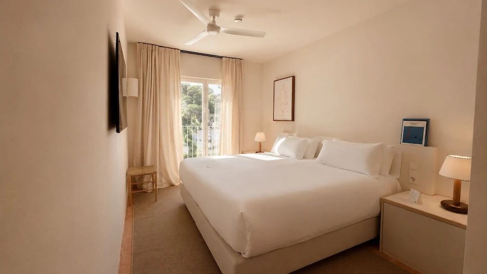 Hell gestaltetes Hotelzimmer mit Deckenventilator, Doppelbett und Zugang zum Balkon.