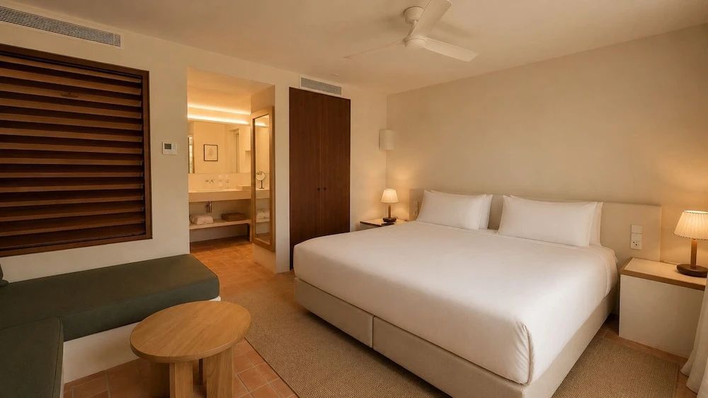 Doppelbett in einem hell eingerichteten Hotelzimmer mit Blick zum angrenzenden Badezimmer.