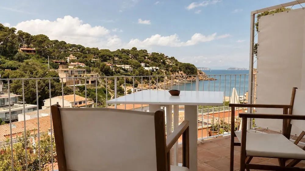Balkon mit weißem Tisch und Stühlen sowie Weitblick auf Hügel und das Meer