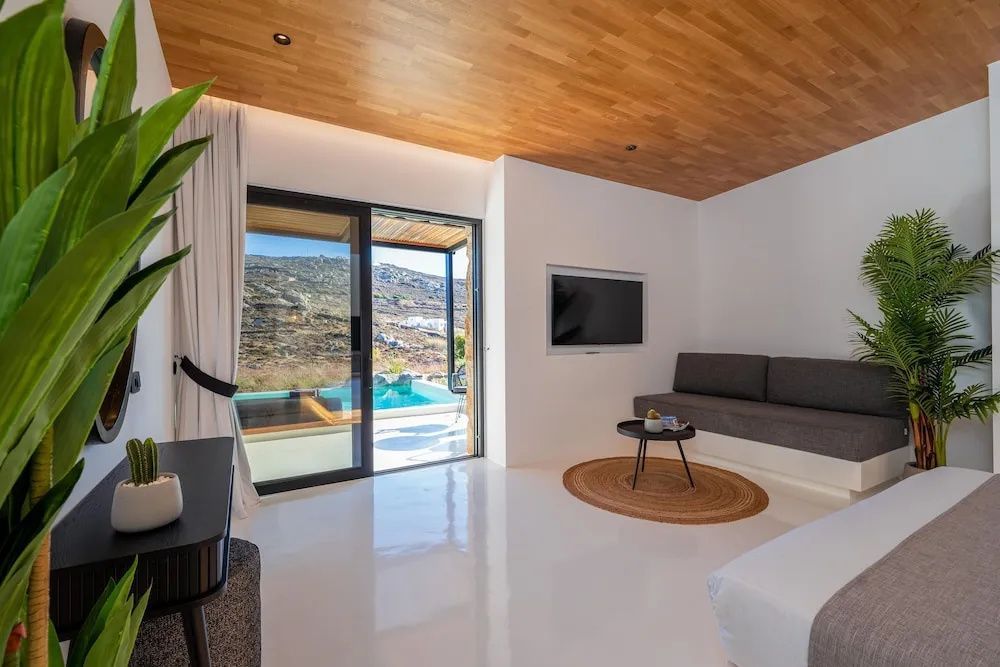Hell eingerichtetes Zimmer mit Holzdecke, Fernseher und Glasschiebetür zum Pool.