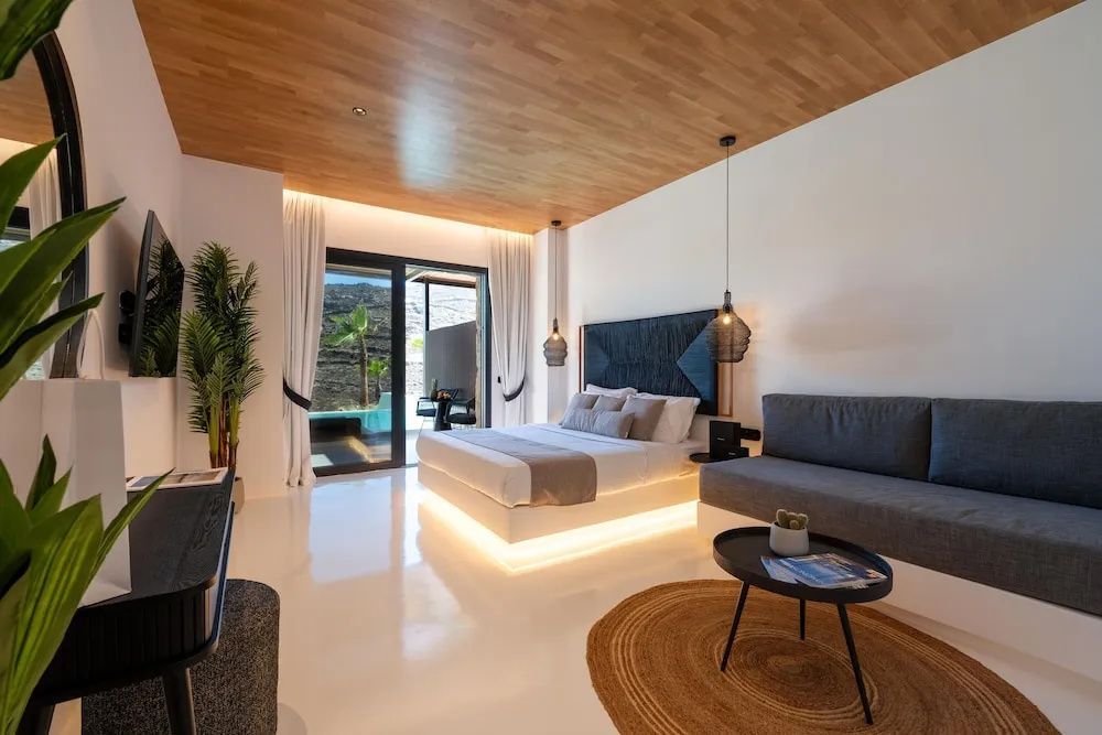 Modernes Hotelzimmer mit Kingsize-Bett, Sofa, Decke aus Holz und Zugang zur Terrasse mit Pool.