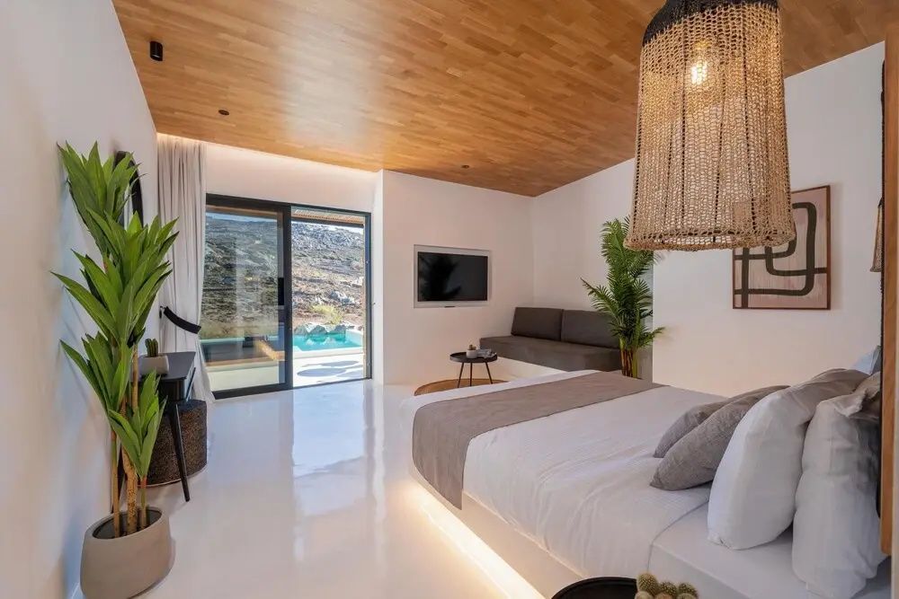Schlafzimmer mit beleuchtetem Doppelbett, Holzdecke, Sofa und Blick auf den Pool.