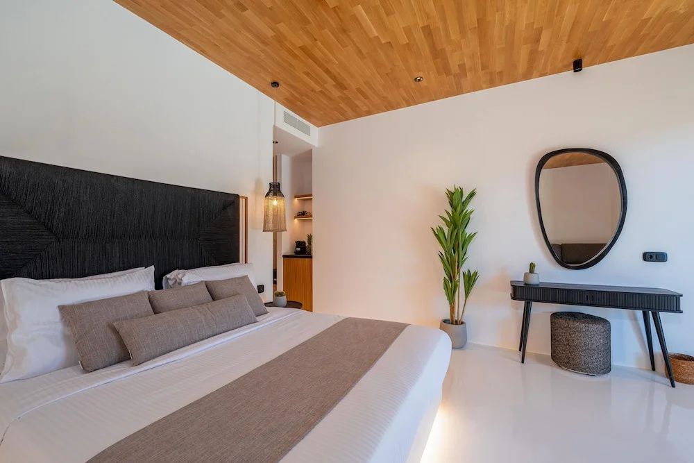 Blick auf das Doppelbett, eine Holzdecke, eine Pflanze und einen Schminktisch.