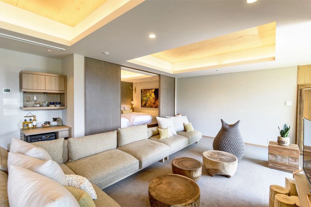 Geräumiger Wohnbereich einer Suite mit großem Sofa, Holzbeistelltischen und Blick ins Schlafzimmer.