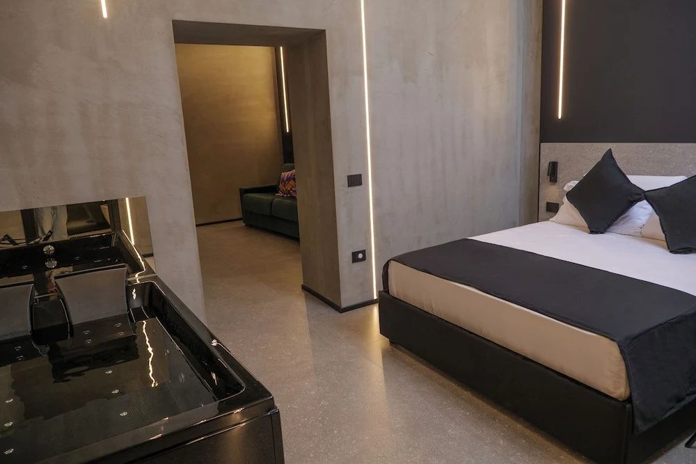 Modernes Hotelzimmer mit Doppelbett, Betonwänden und Blick in den Wohnbereich.
