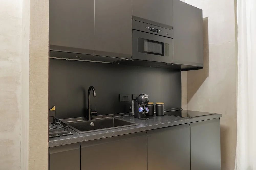 Dunkle Küchenzeile mit Spülbecken, Kaffeemaschine und Mikrowelle.