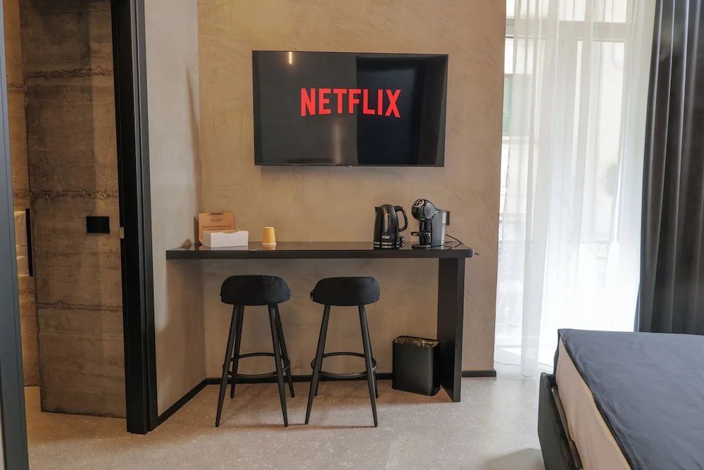 Sitzecke im Hotelzimmer mit zwei Barhockern, Tresen, Wasserkocher und Fernseher an der Wand.