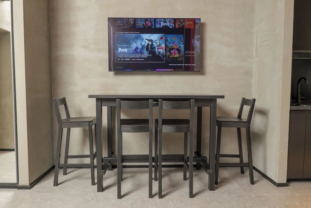 Dunkler hoher Tisch mit vier Barstühlen unter einem montierten Wandfernseher.