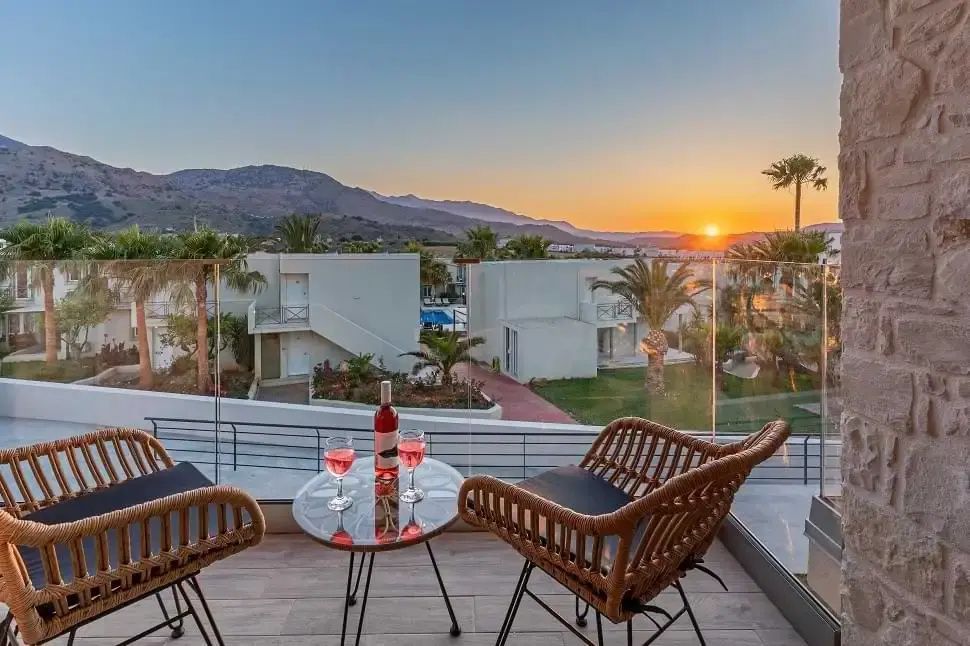 Balkon mit zwei Stühlen und einem Tisch mit Blick auf die Anlage bei Sonnenuntergang.
